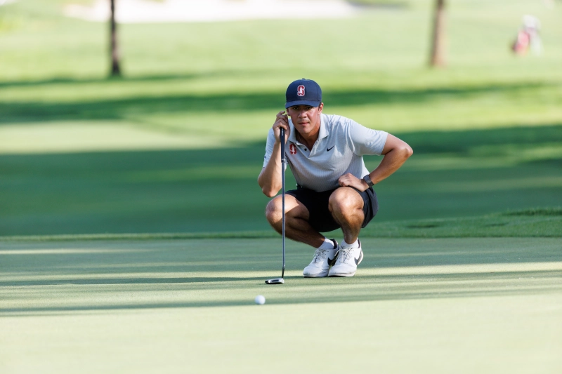 golf player bends down and looks closely at a golf ball after putting it