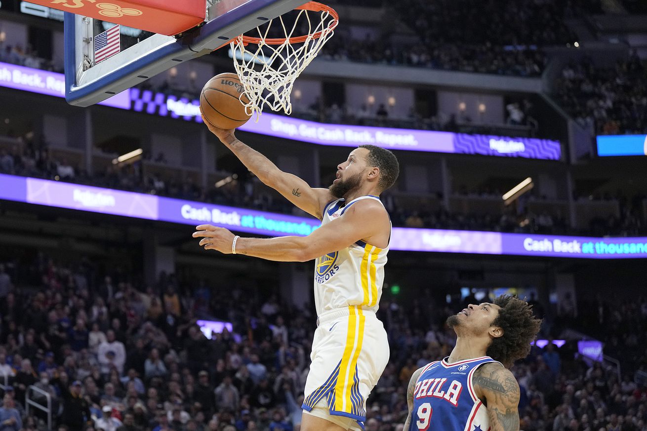 Steph Curry making a layup with Kelly Oubre Jr. behind him. 