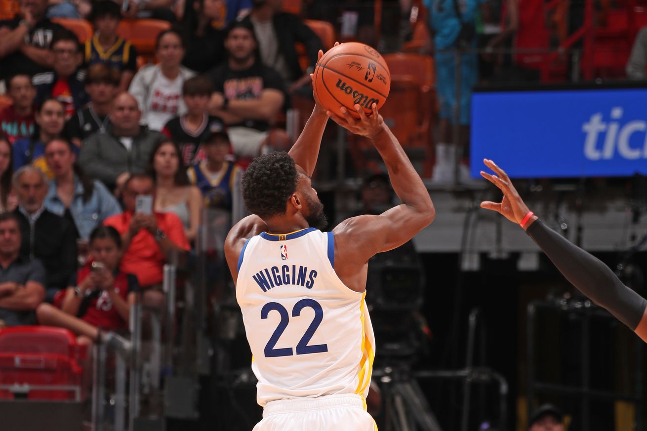 Andrew Wiggins is about to shoot the ball during the game against the Miami Heat at Kaseya Center. An opposing player’s arm reaches to block him. The Warriors are wearing their white jerseys.