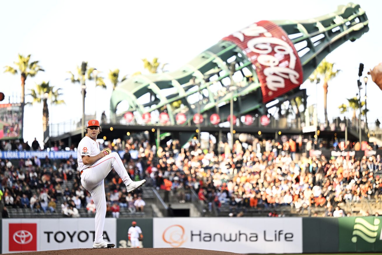 Wide view of Erik Miller throwing a pitch at Oracle Park, with the left field bleachers and large Coke bottle statue in the background. 