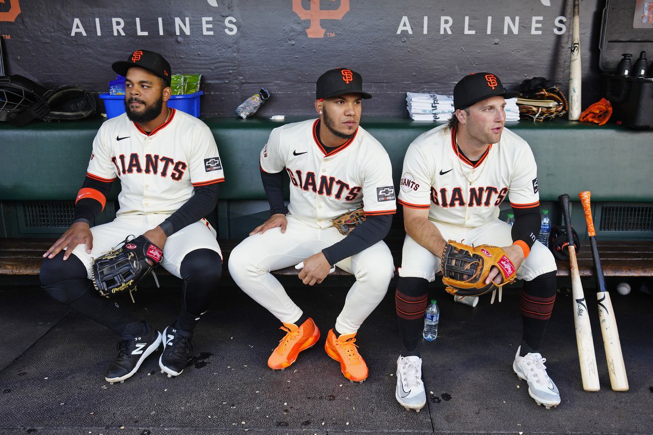 Thairo Estrada and Casey Schmitt sitting next to each other in the dugout, near Heliot Ramos. 