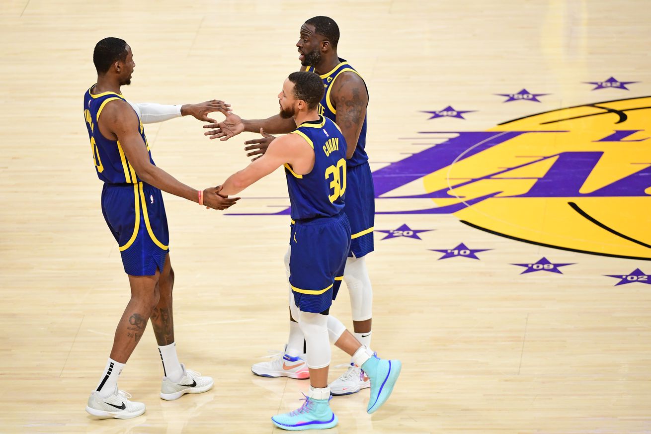 Steph Curry, Draymond Green, and Jonathan Kuminga high-fiving in a circle. 