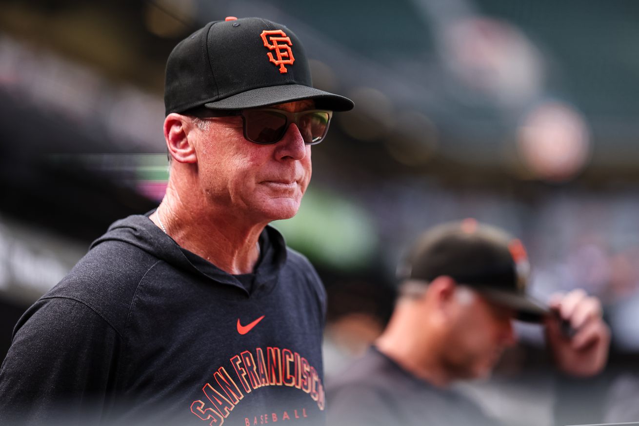 Bob Melvin wearing sunglasses and a hoodie in the Giants dugout. 