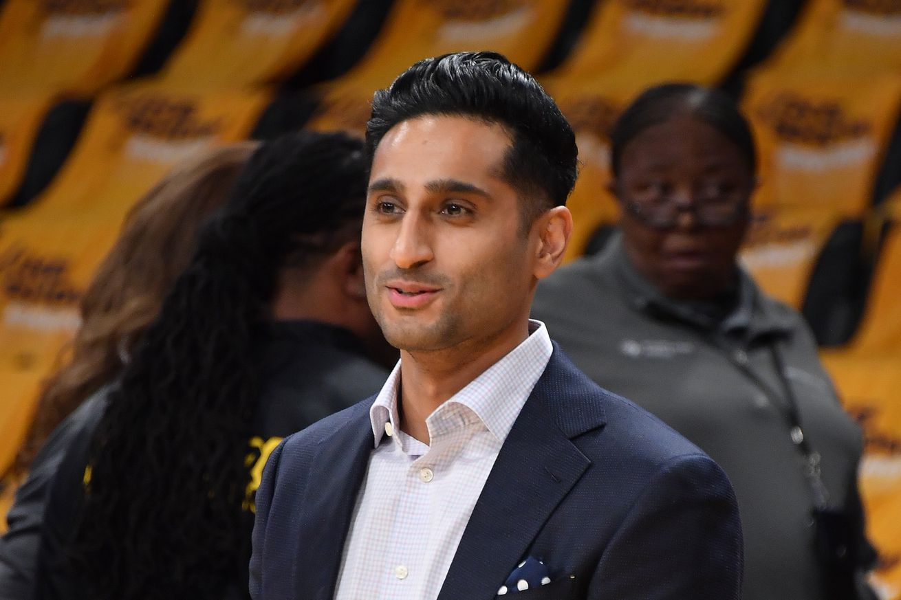 Shams Charania smiling in a suit at a basketball game.