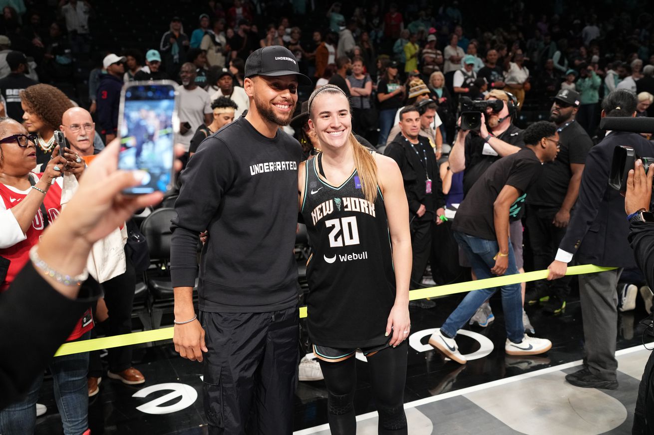 Steph Curry and Sabrina Ionescu smiling for cameras after a Liberty game. 