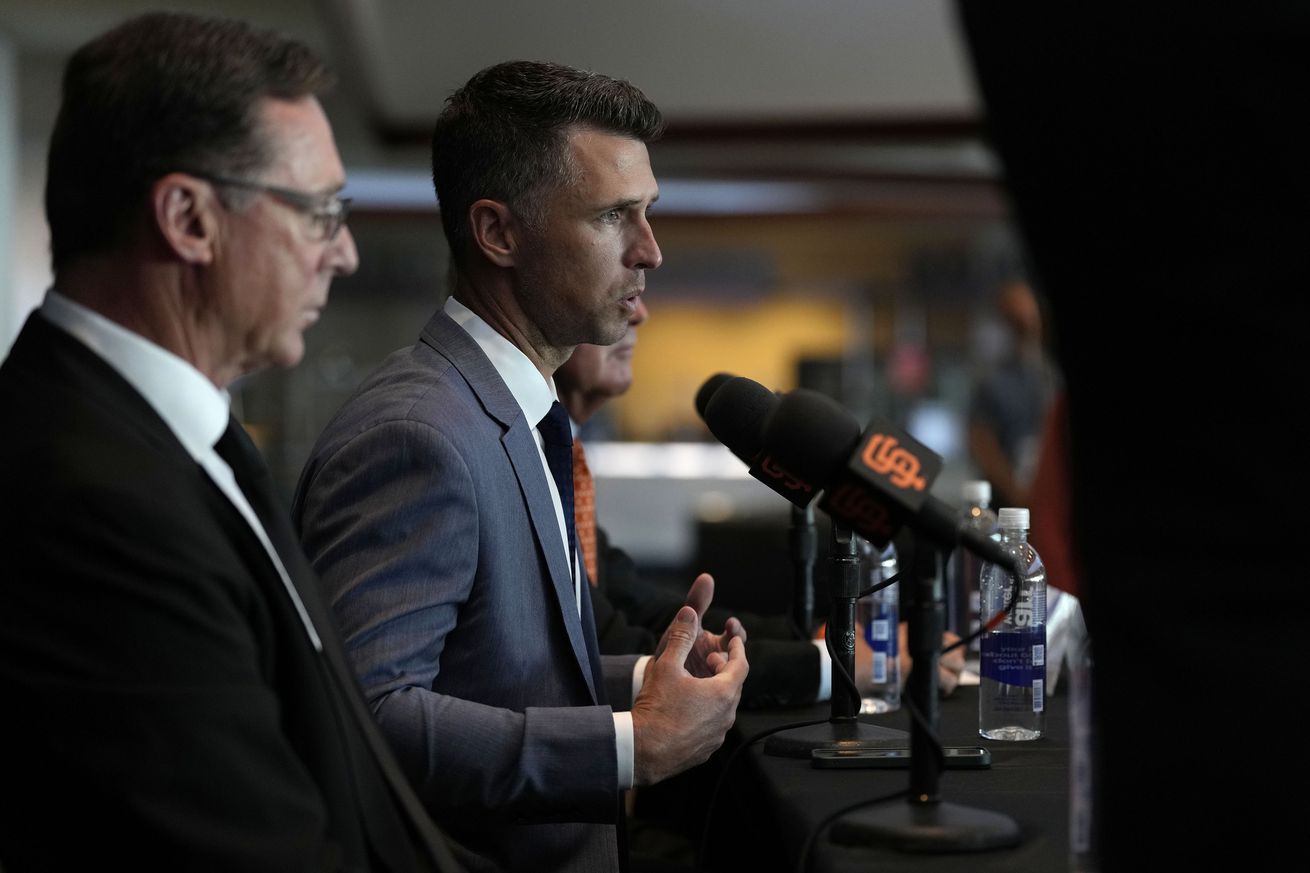 Side view of Buster Posey and Bob Melvin speaking at a press conference. 