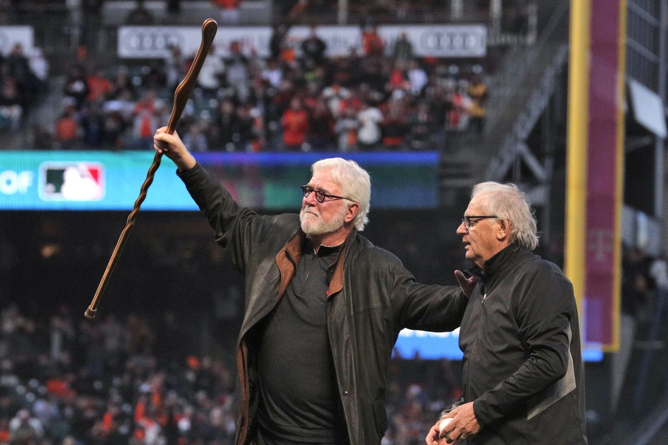 Mike Krukow pointing to the stands while standing next to Duane Kuiper on the field. 