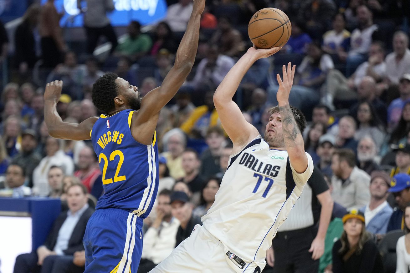 Luka Dončić shooting a fadeaway jumper over the outstretched arm of Andrew Wiggins.