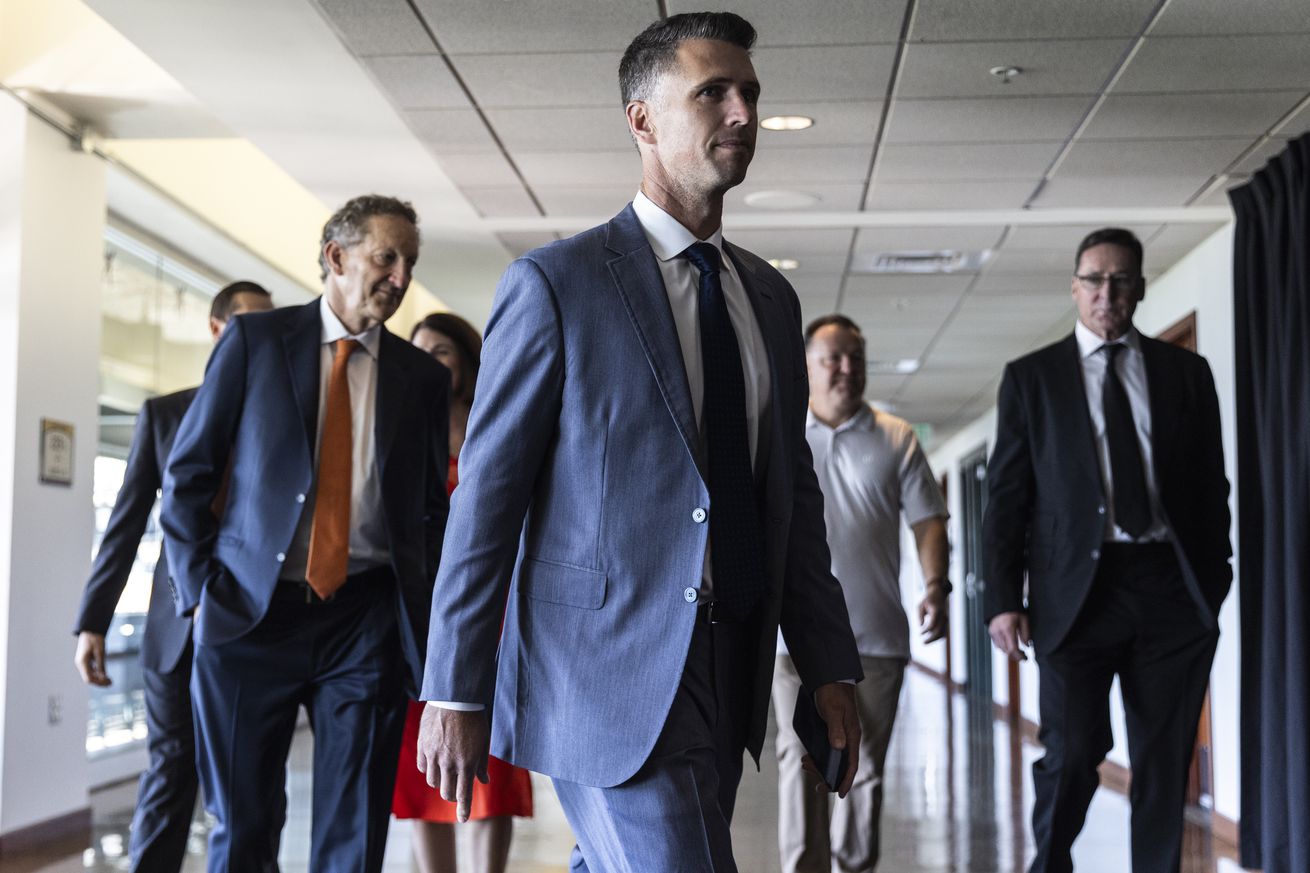 Buster Posey walking in front of a group of Giants execs. 