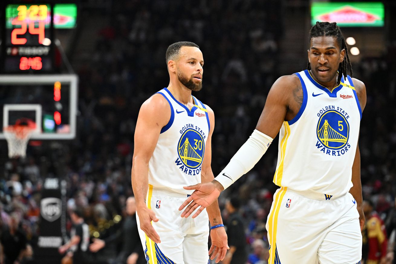 Steph Curry and Kevon Looney walking side by side and reaching out to slap hands. 