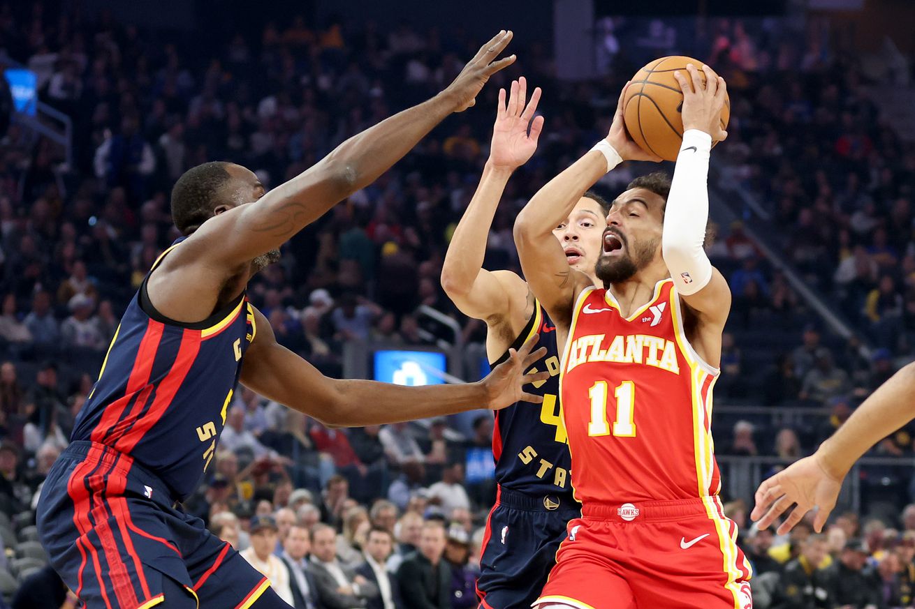 Draymond Green and Lindy Watters III surrounding Trae Young, who is holding the ball. 