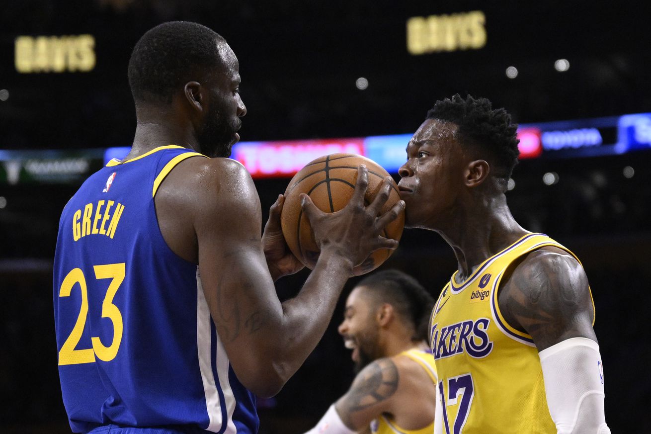 Draymond Green, in a Warriors jersey, holding a ball to the face of Dennis Schröder, in a Lakers jersey, while intensely staring at each other. 