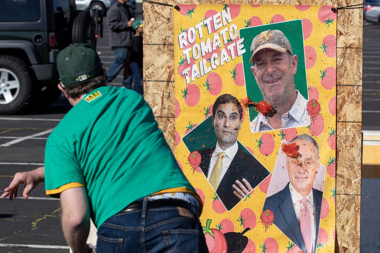 Disgruntled Oakland Athetics fans thow tomatoes at photos of Steve Fisher, Dave Kaval and Rob Manfred