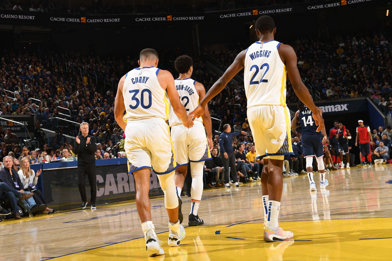 View from behind of Steph Curry and Andrew Wiggins slapping hands, walking behind Trayce Jackson-Davis. 