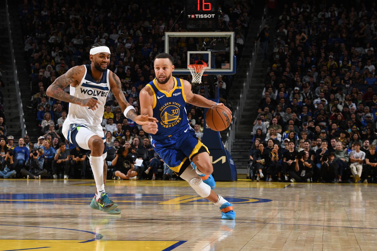 Stephen Curry dribbling by a Wolves defender with his left hand. 