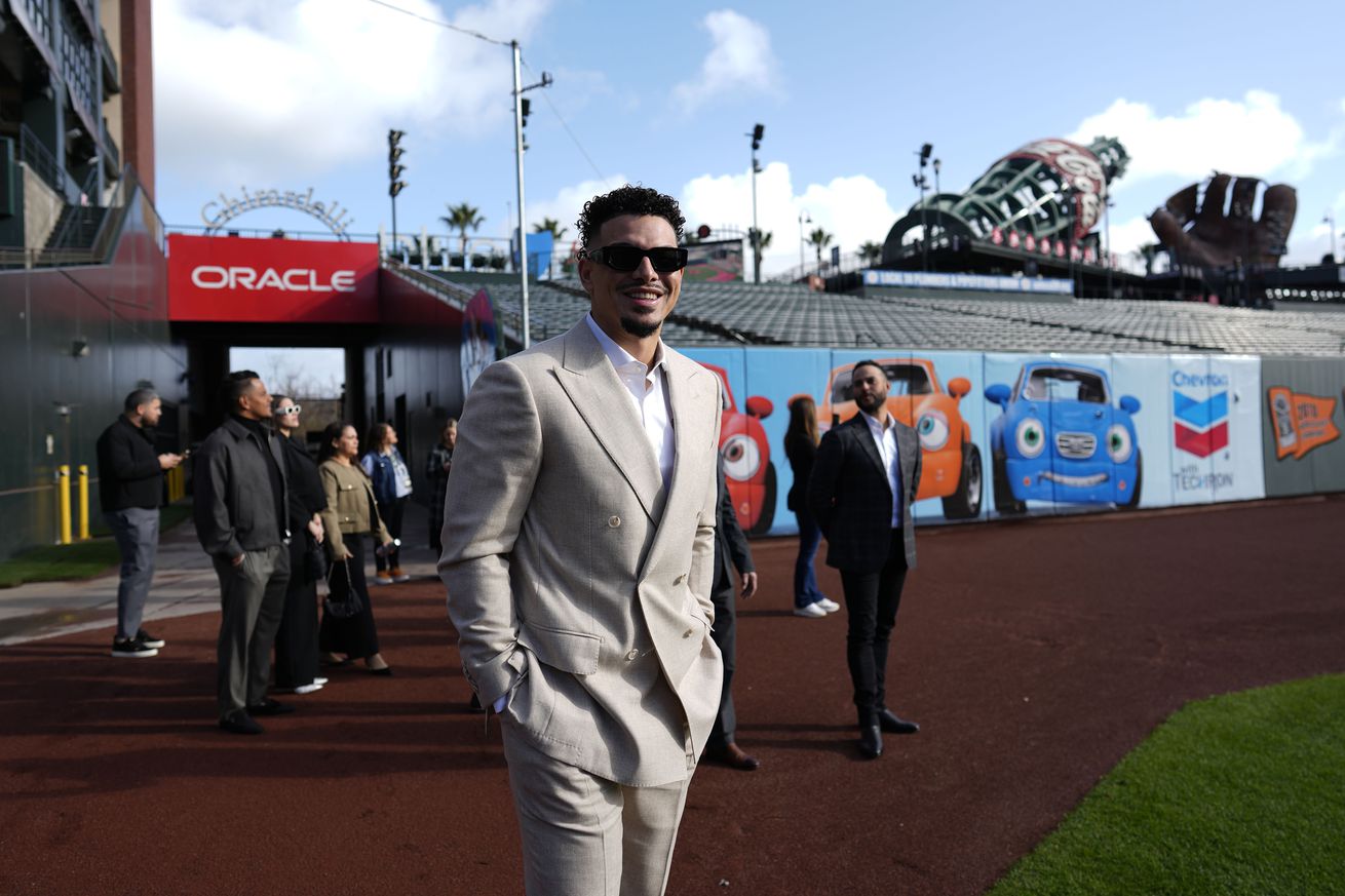 Willy Adames smiling in a suit on the Giants field. 