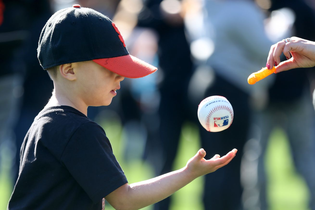 A kid in a Giants hat tossing the ball in the air. 