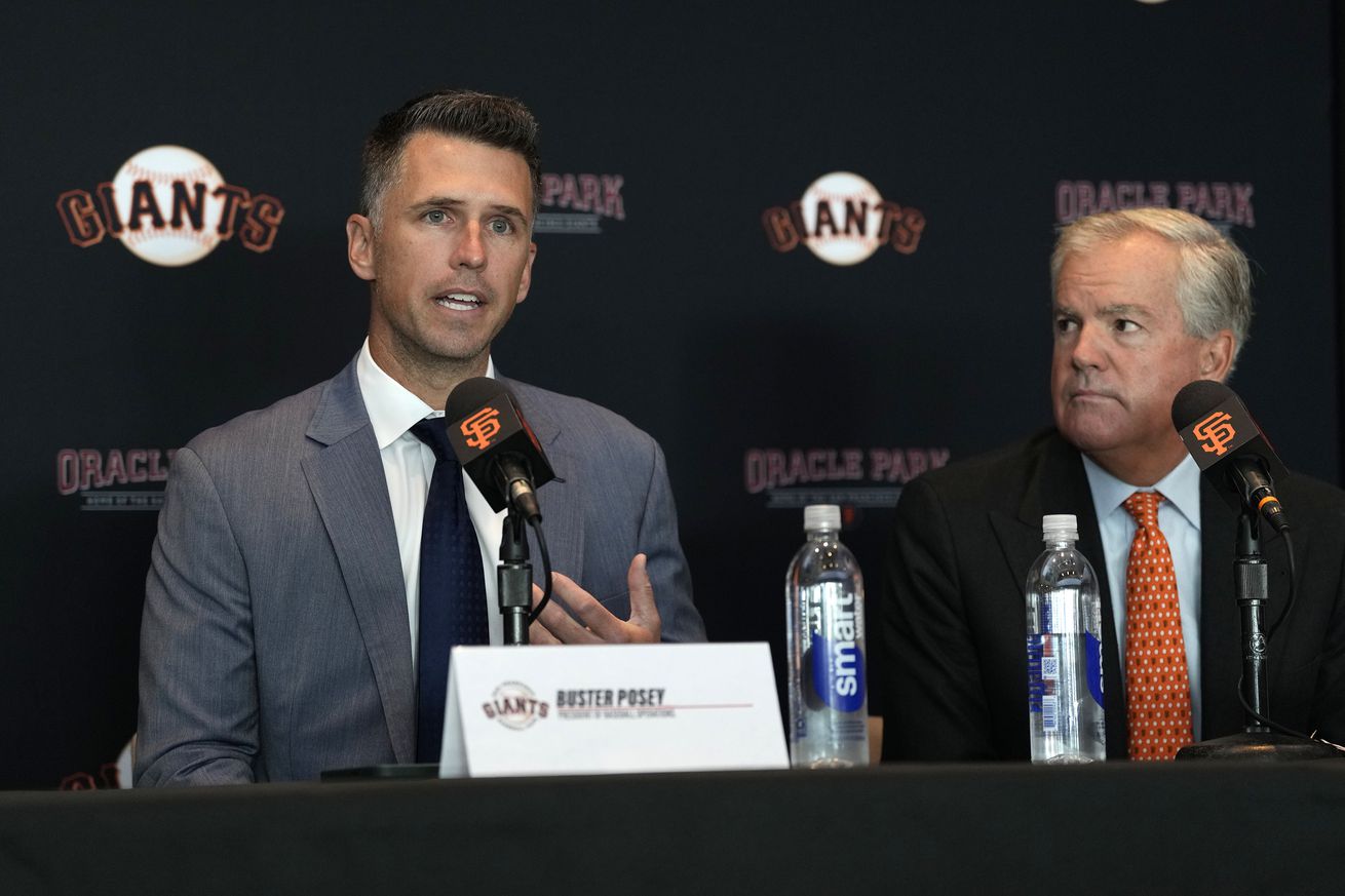 Buster Posey speaking at a press conference next to Greg Johnson. 