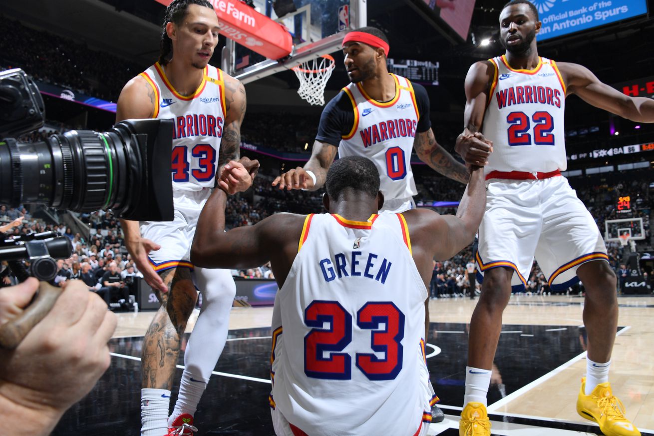 Draymond Green sitting on the court flexing as Gary Payton II, Andrew Wiggins, and Lindy Waters III help him up. 