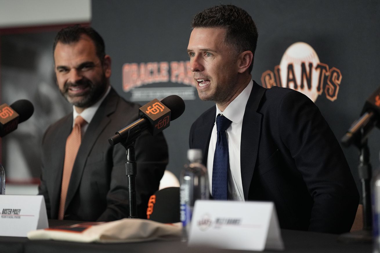 Buster Posey speaking at a press conference next to Zack Minasian. 