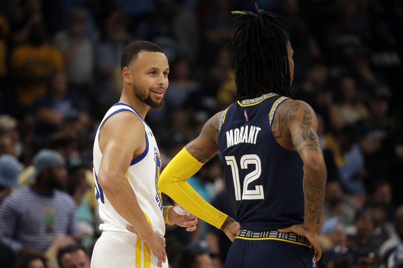 Steph Curry and Ja Morant standing side-by-side during a game, talking. 