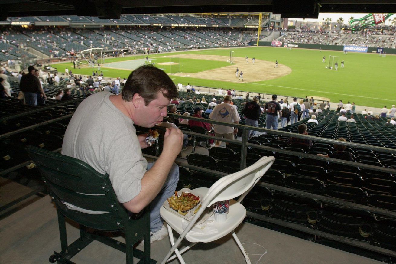 A fan eating food off of a chair used as a table at Oracle Park. 