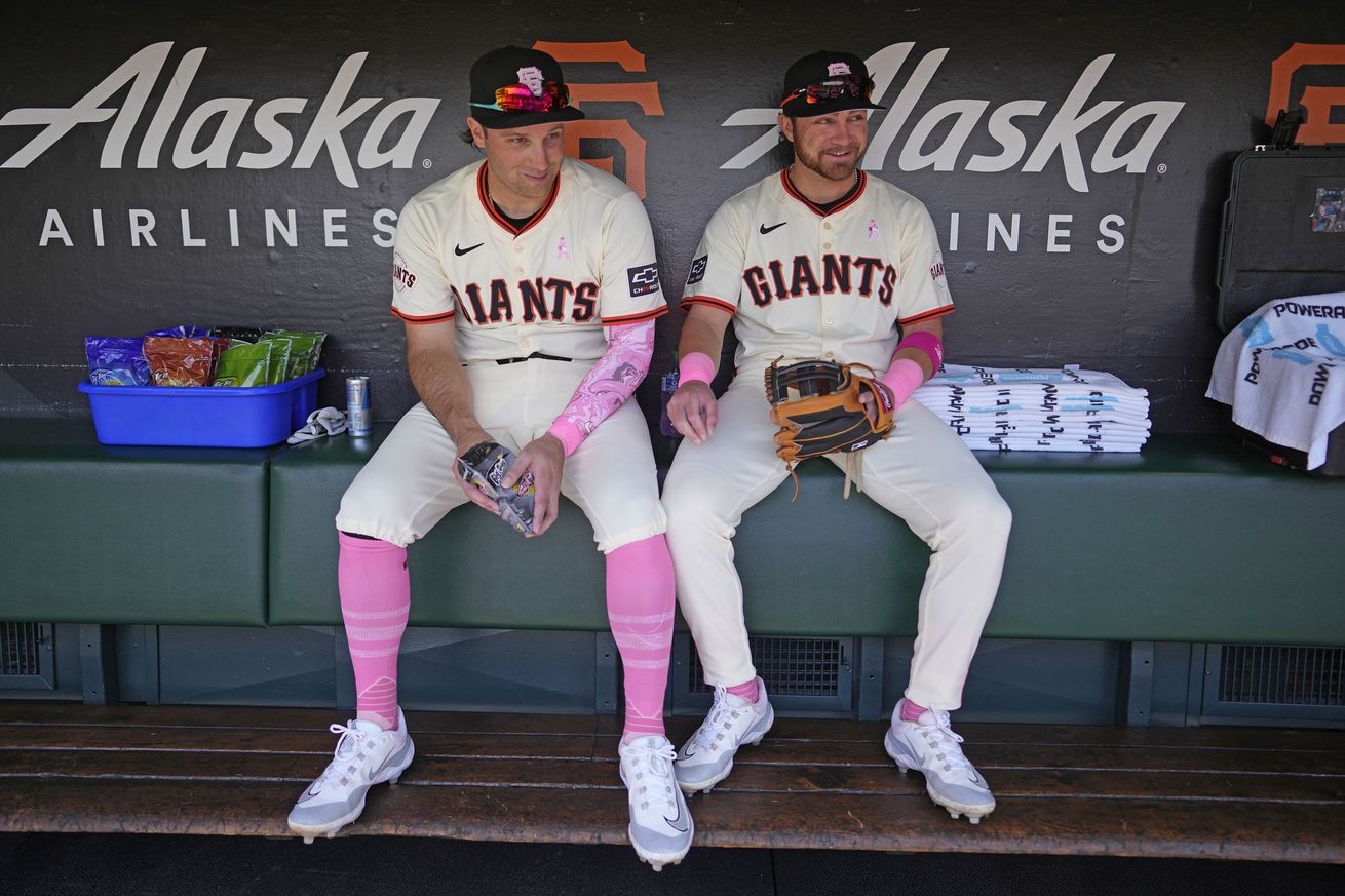 Casey Schmitt sitting next to Brett Wisely on the bench, wearing Giants jerseys and pink socks and arm bands. 