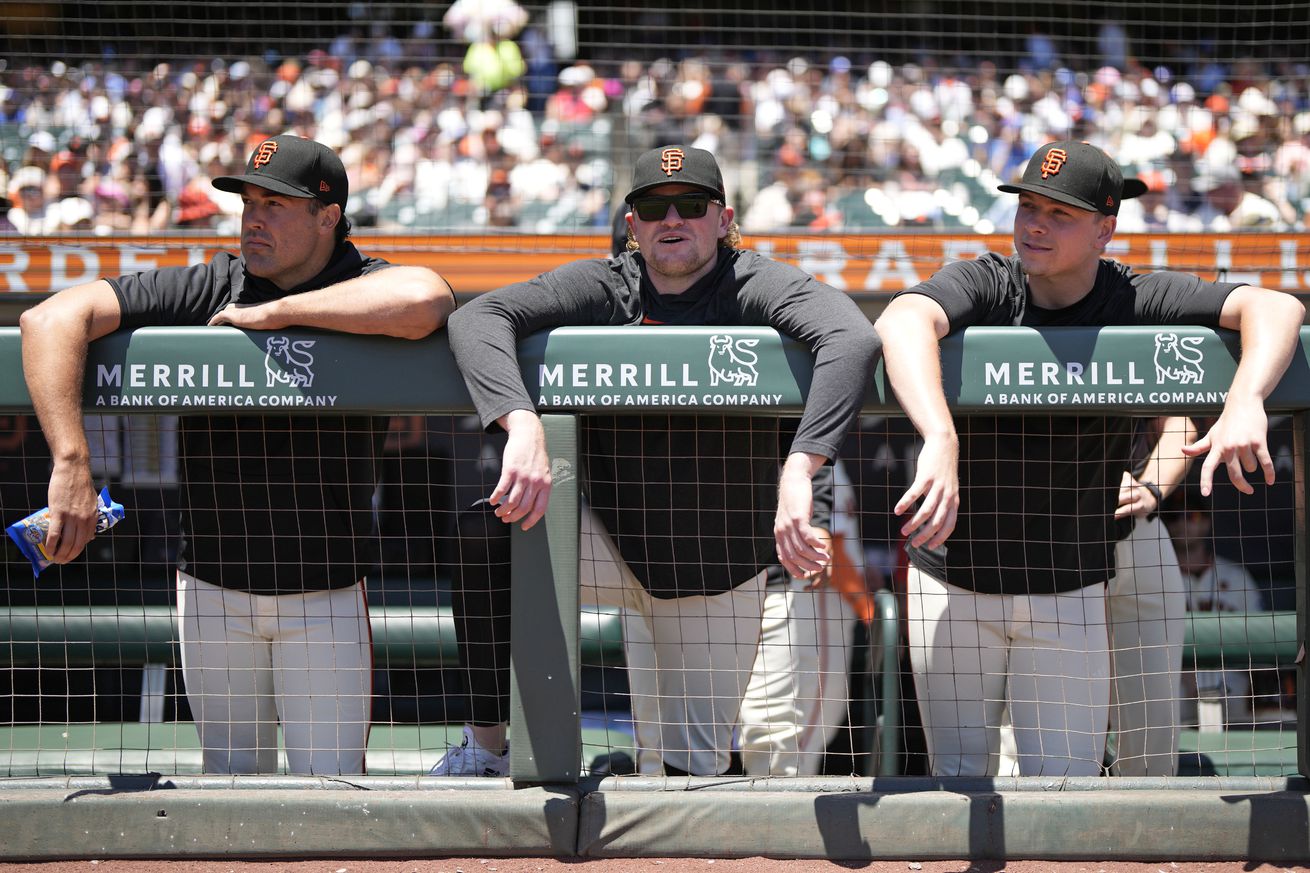 Robbie Ray, Logan Webb, and Kyle Harrison leaning over the dugout railing.