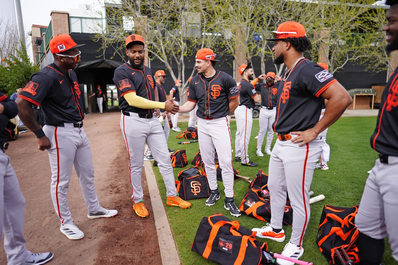 Marco Luciano, Jerar Encarnación, Willy Adames, and Luis Matos talking at Spring Training, surrounded by bags and equipment. 