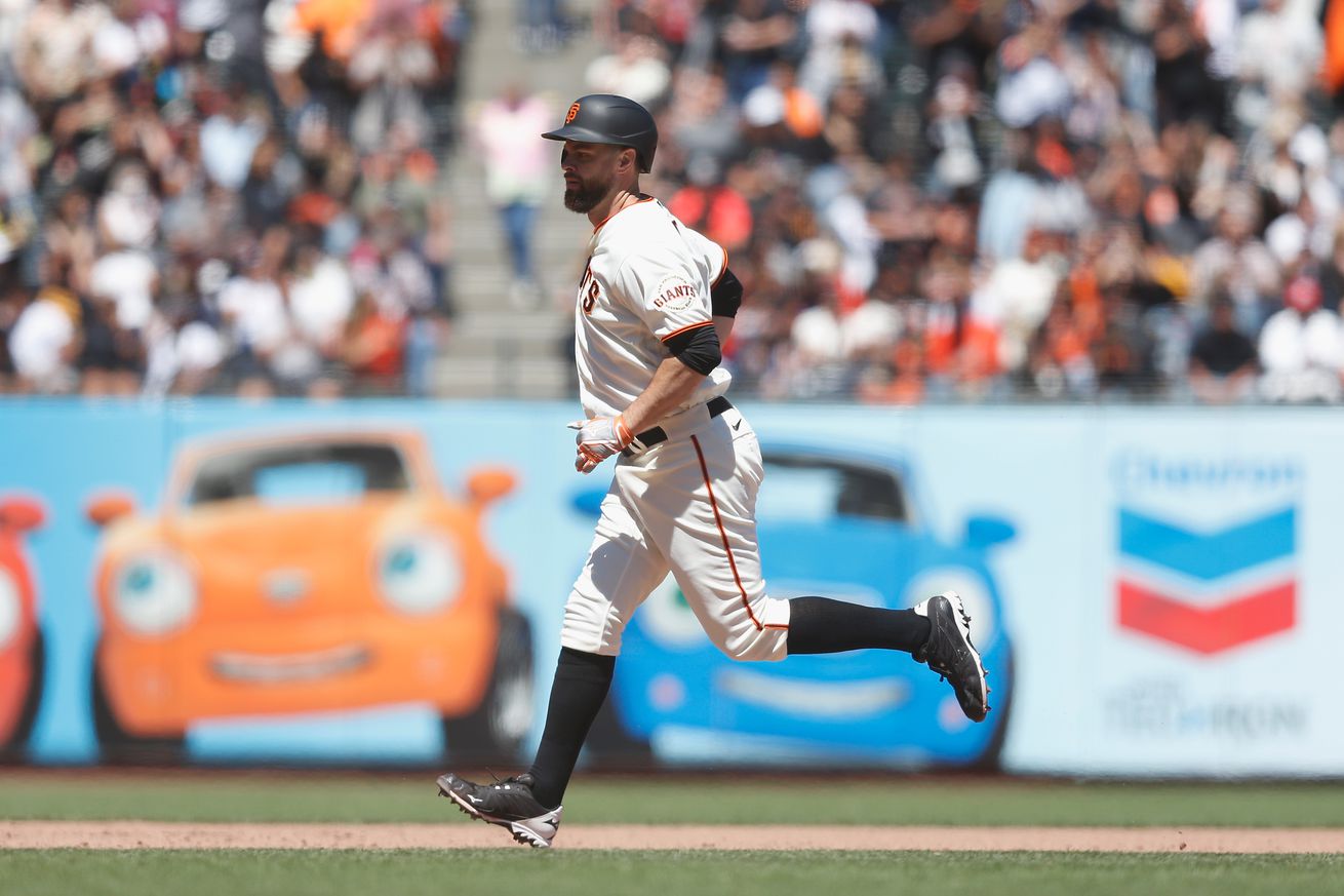 Brandon Belt jogging the bases with the Giants outfield wall Chevron cars in the background. 