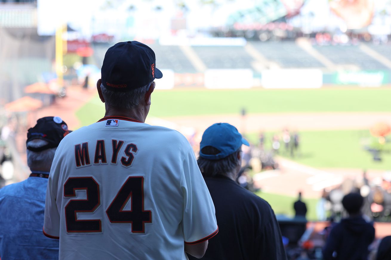 View from behind of a fan wearing a Willie Mays jersey looking out at the field at Oracle Park. 