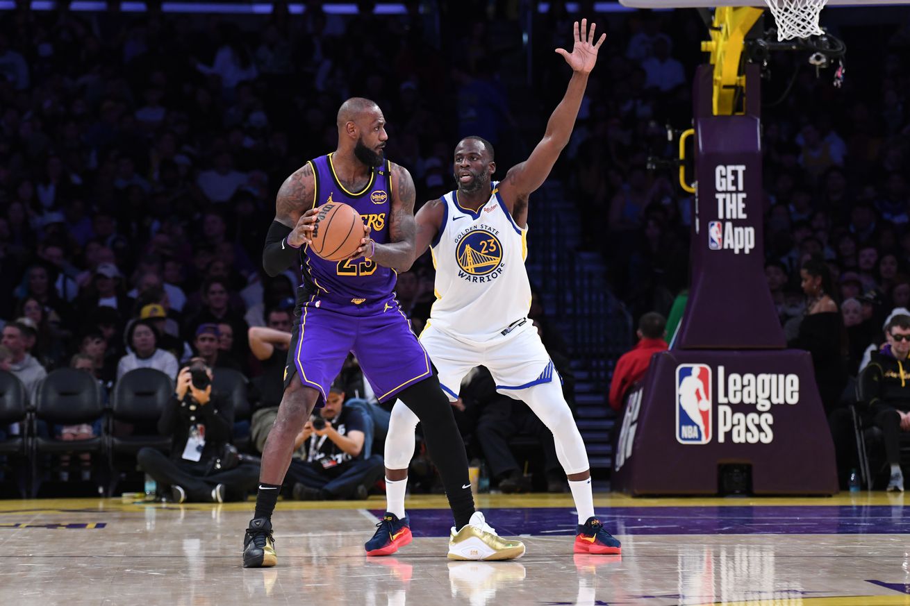 LeBron James holding the ball, with his back to the basket, while Draymond Green defends with his arms raised high. 