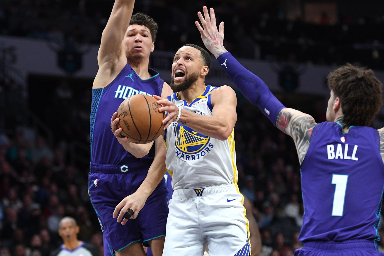 Steph Curry attempting a layup between two Hornets defenders. 