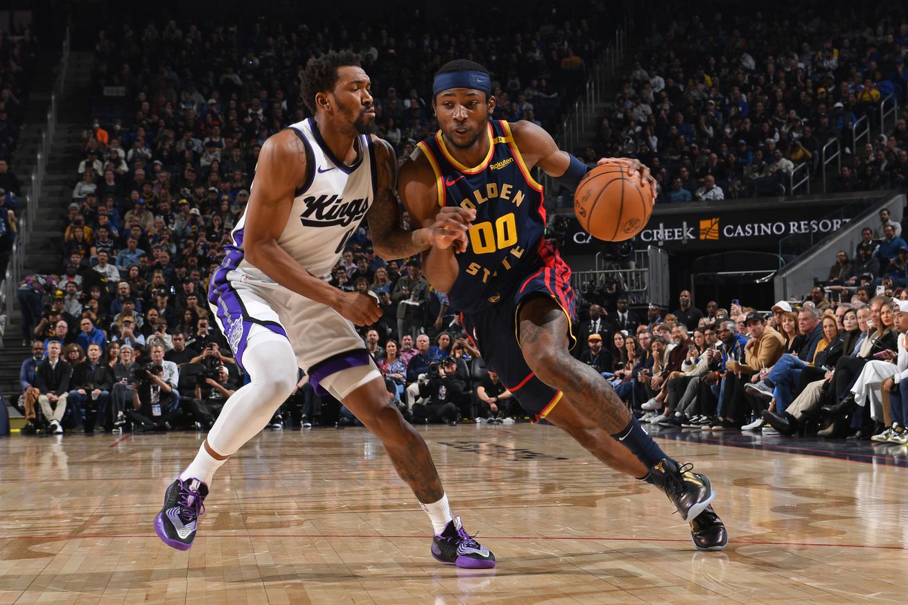 Jonathan Kuminga dribbling with his left hand around a Kings defender. 