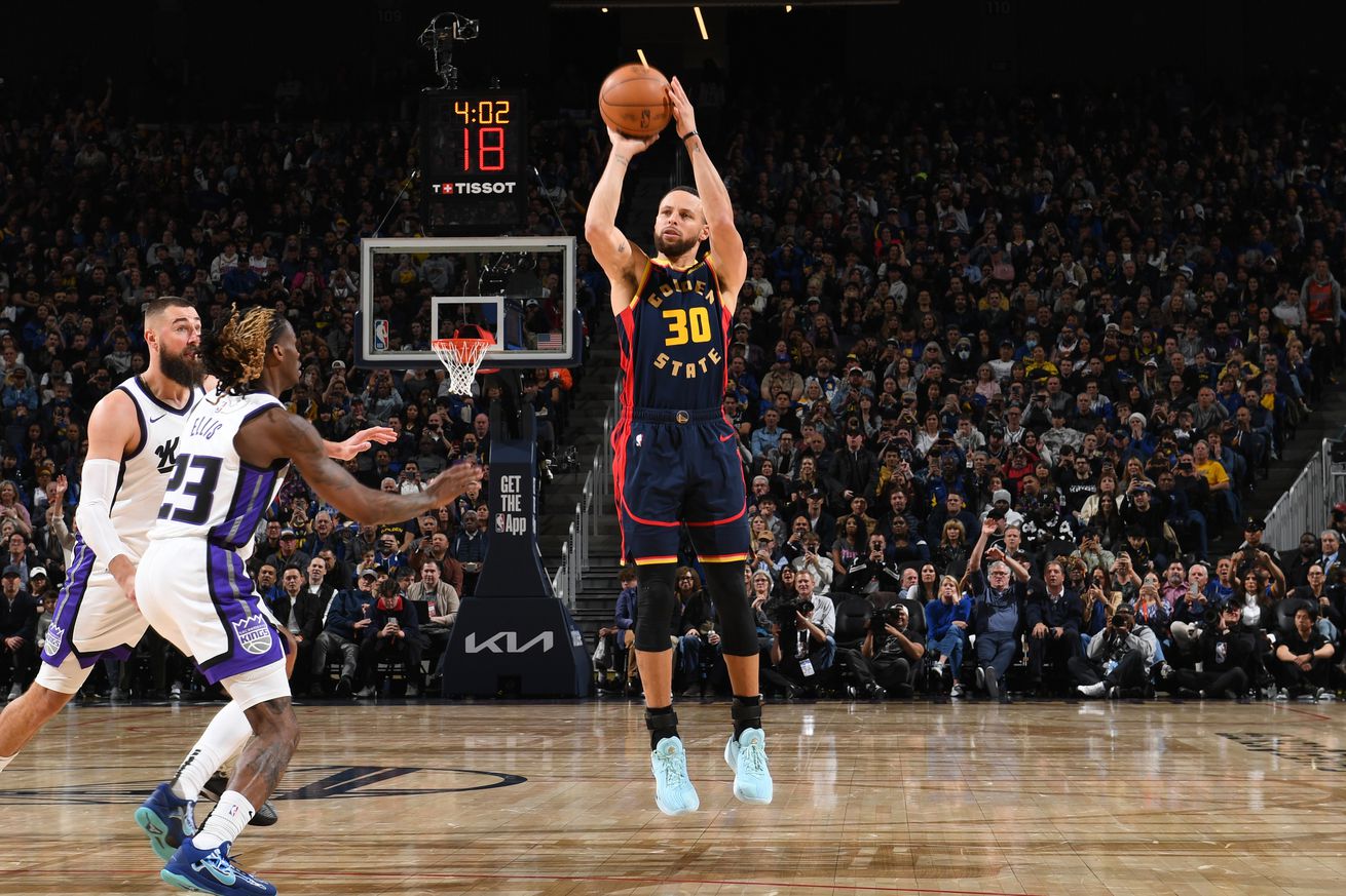 Steph Curry shooting a three as two Kings defenders chase him. 