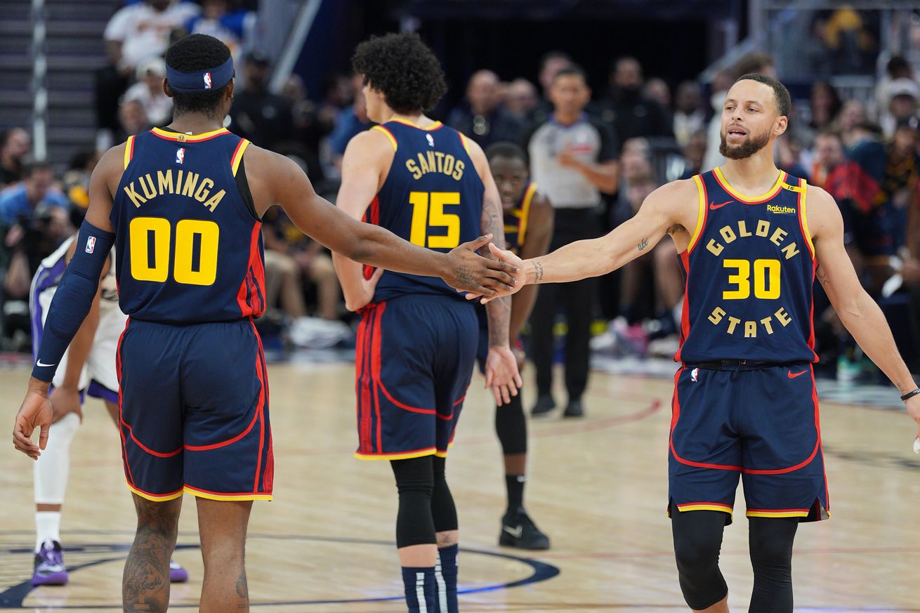 Steph Curry slapping hands with Jonathan Kuminga, with Gui Santos in the background. 