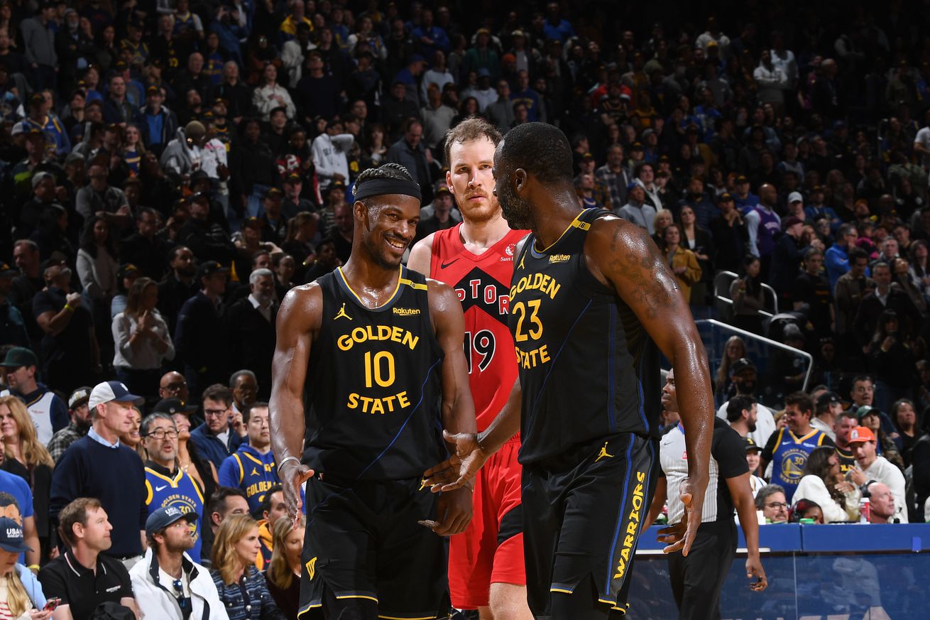 Jimmy Butler III and Draymond Green talking and smiling on the court, with Jakob Poeltl behind them. 